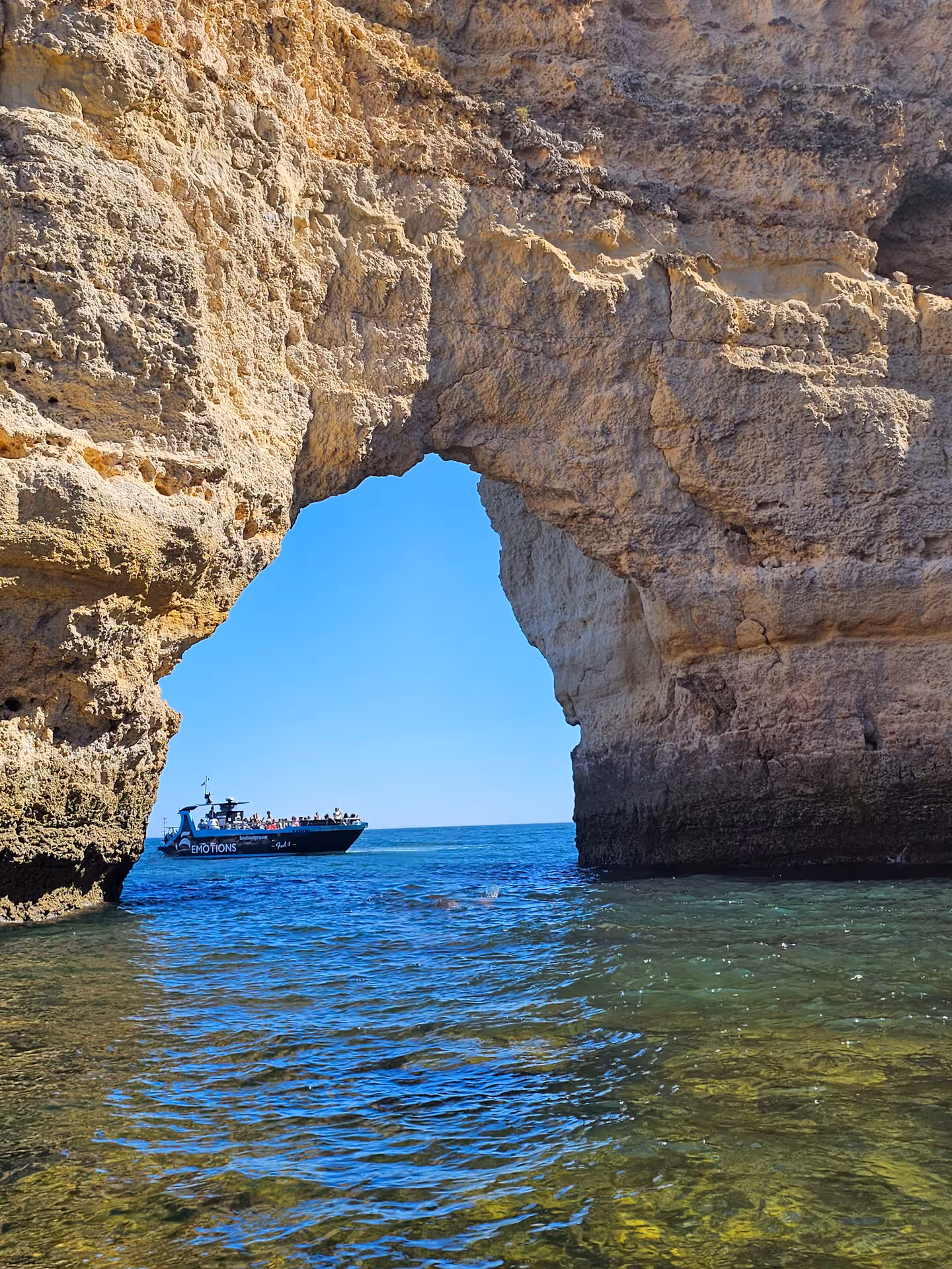 A boat navigates through a natural arch on the Algarve Coast, offering breathtaking views of the sea.