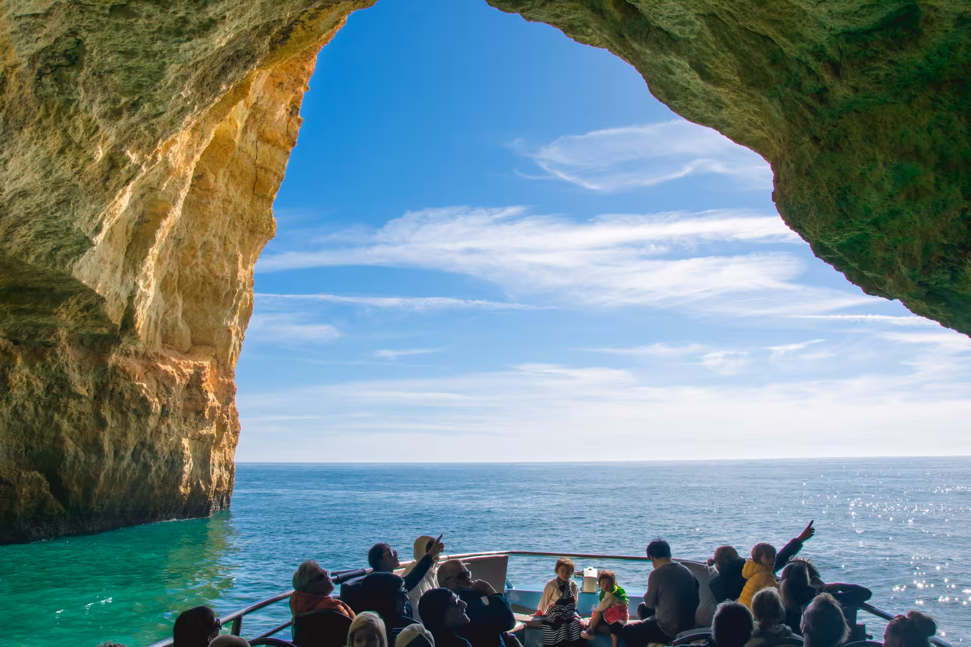 Tourists enjoy a boat tour exploring the stunning Benagil Caves along the Algarve Coast under a clear blue sky.