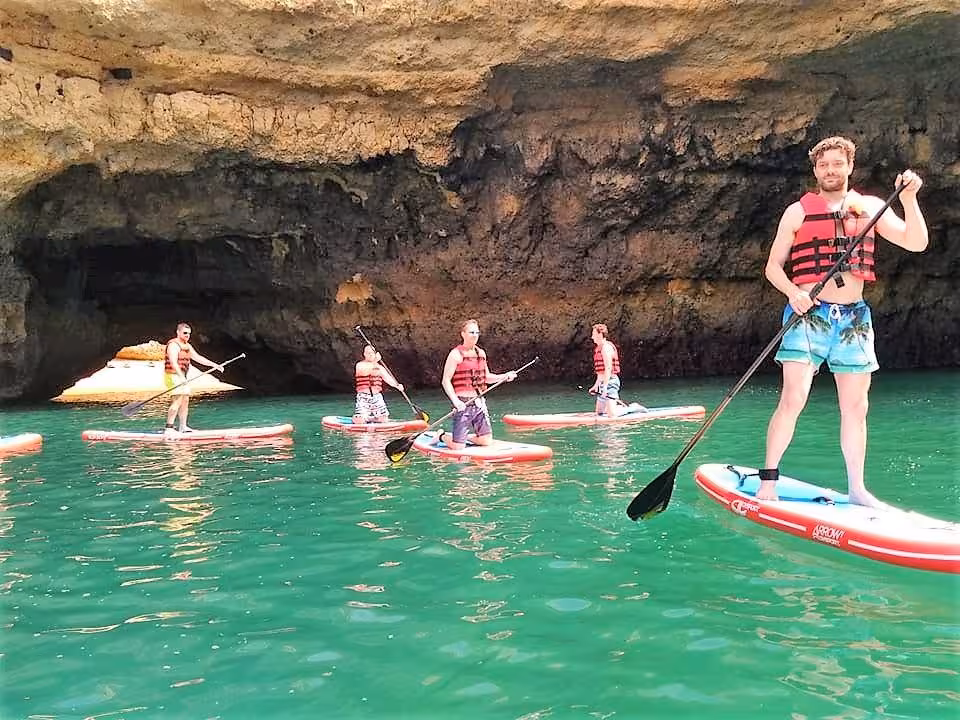 Group of paddleboarders wearing life vests exploring dramatic Albufeira sea caves on a guided SUP tour