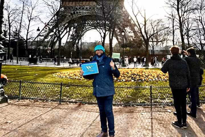 Visitor posing under the Eiffel Tower in Paris, ideal for Eiffel Tower dining experience with lunch or dinner upgrades.