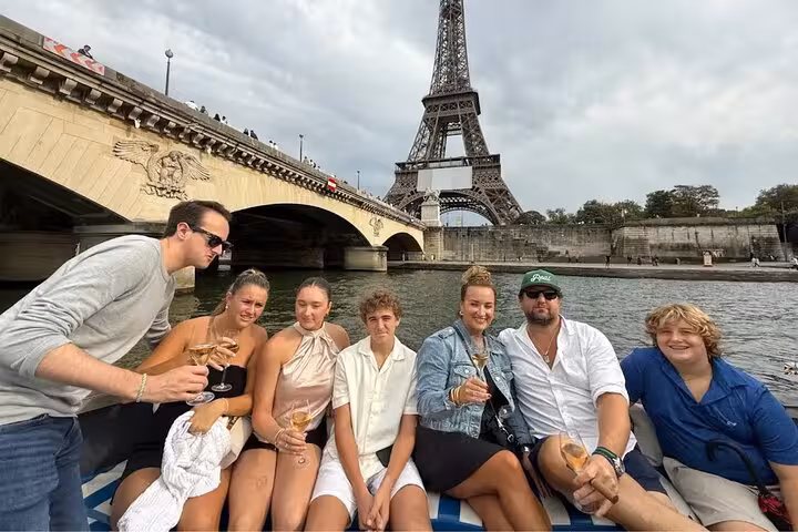 Group toasting champagne on Seine cruise near Eiffel Tower, Paris dinner upgrade experience by boat
