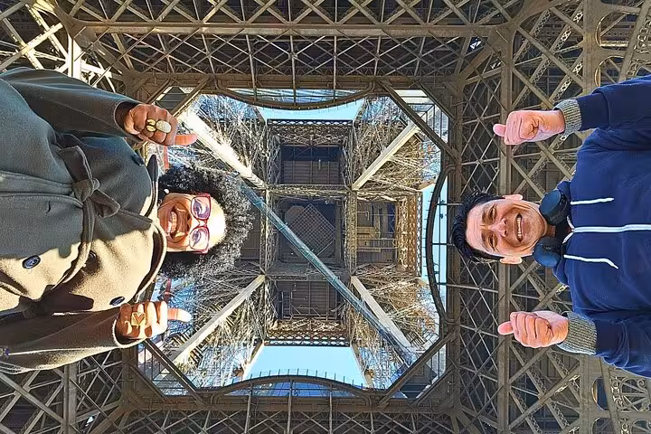Visitors pose under the Eiffel Tower on a dining experience tour with lunch or dinner upgrade in Paris