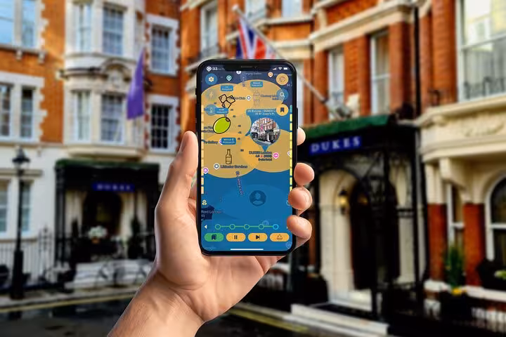 Hand holding a smartphone with James Bond walking tour app game map near Dukes Hotel in London