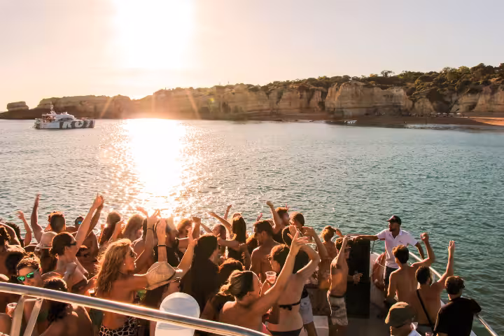 Lively Lagos boat party with crowds dancing at sunset near stunning Algarve cliffs and golden coastline.