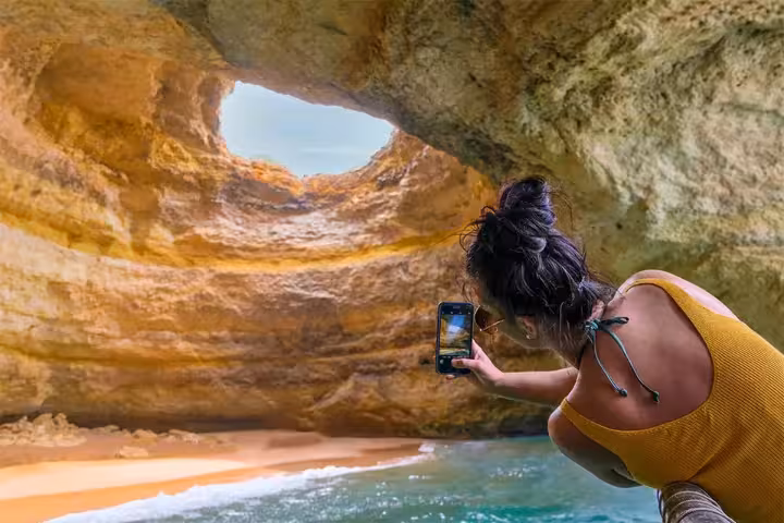 Tourist photographing the stunning golden rock interior of Benagil Cave on an Algarve catamaran tour from Portimao