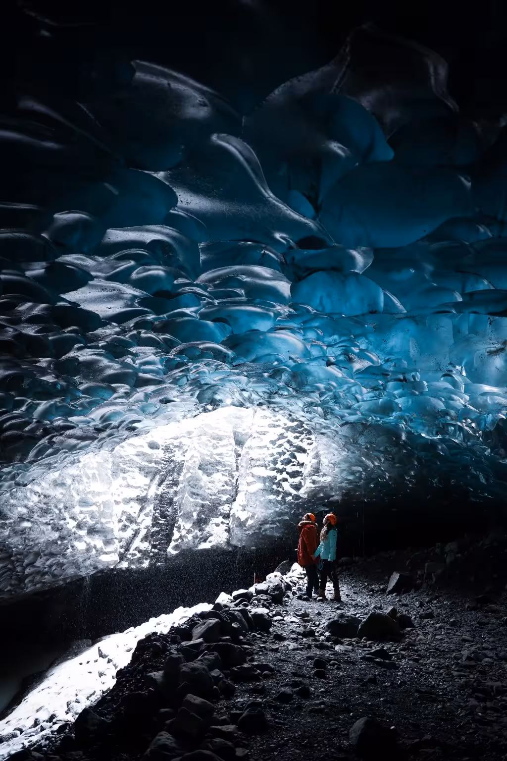 Two tourists in bright jackets marvel at the breathtaking blue ice ceiling inside Vatnajokull glacier cave Iceland