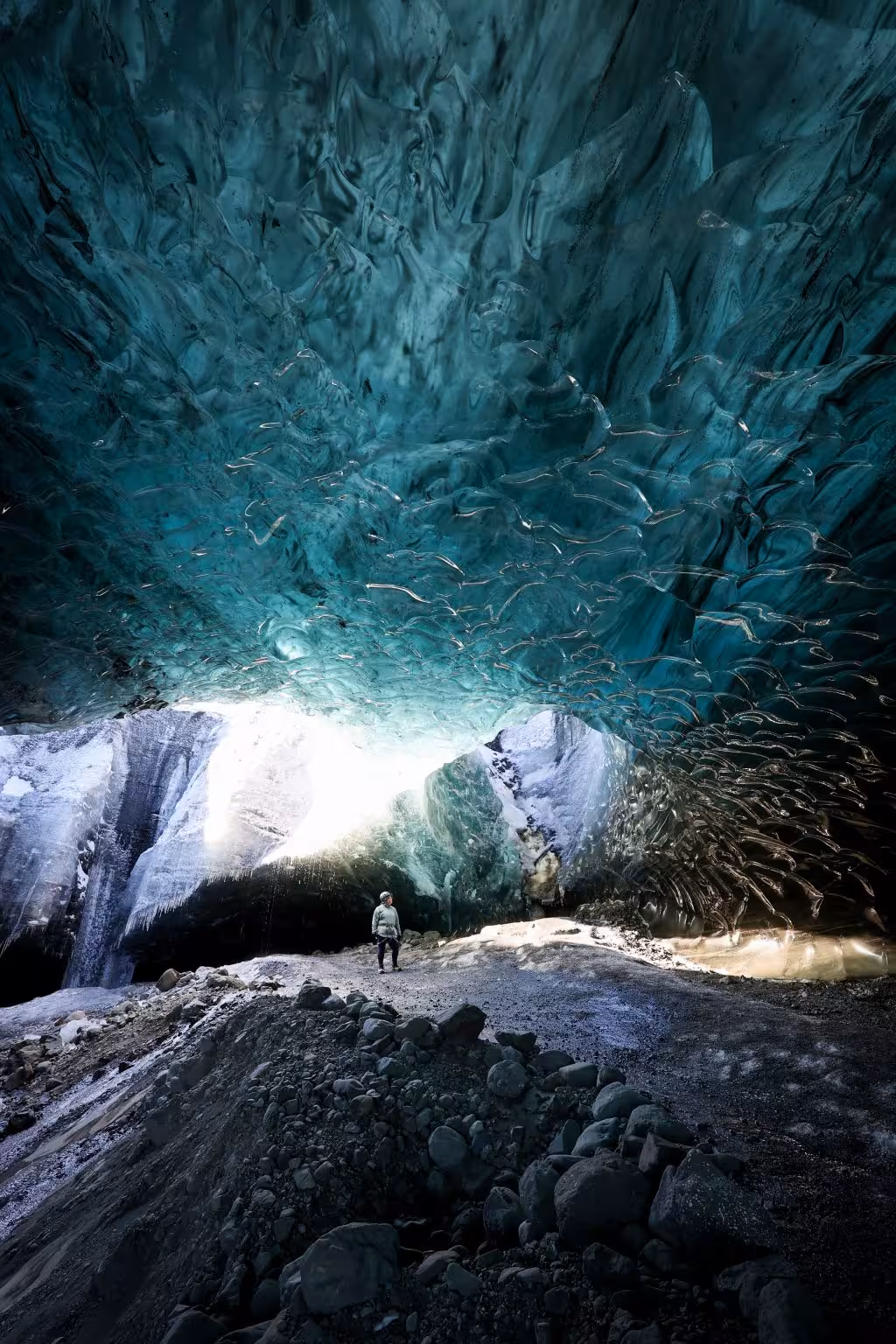 A lone explorer stands beneath the stunning turquoise ice ceiling of Vatnajokull glacier cave in Iceland.