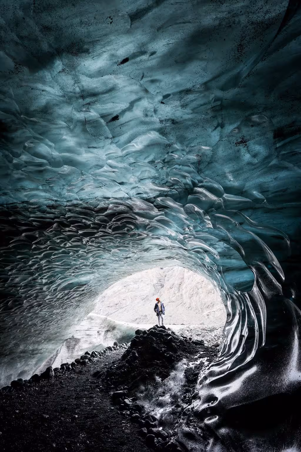 A visitor in a red helmet gazes at the breathtaking blue ice tunnel interior on a Vatnajokull guided cave tour.