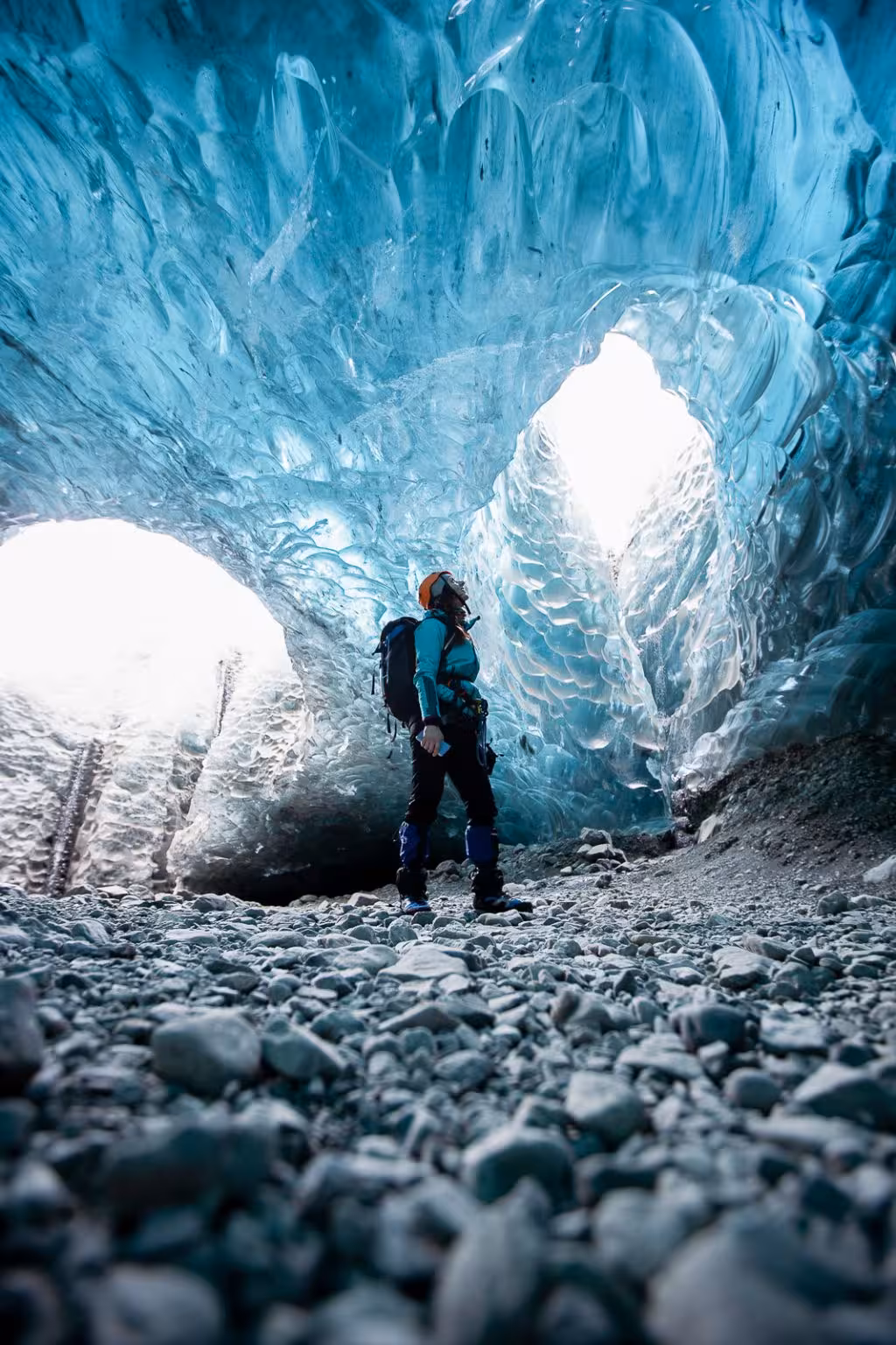 Explorer in full gear gazing up at breathtaking blue ice arches inside Vatnajokull ice cave on a guided Iceland tour
