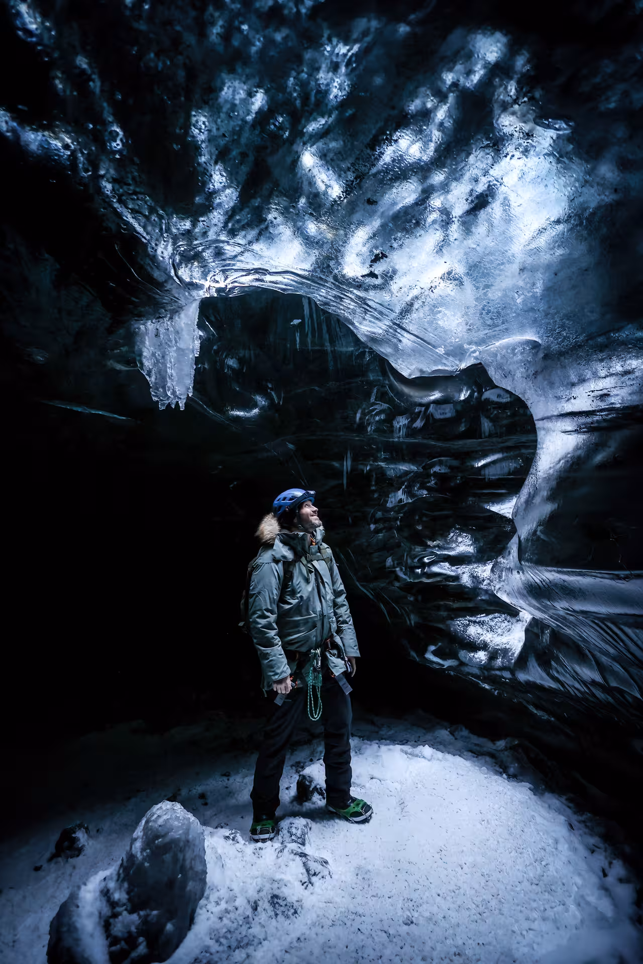 A helmeted explorer gazes up at dramatic dark ice cave walls on a Vatnajokull glacier adventure tour