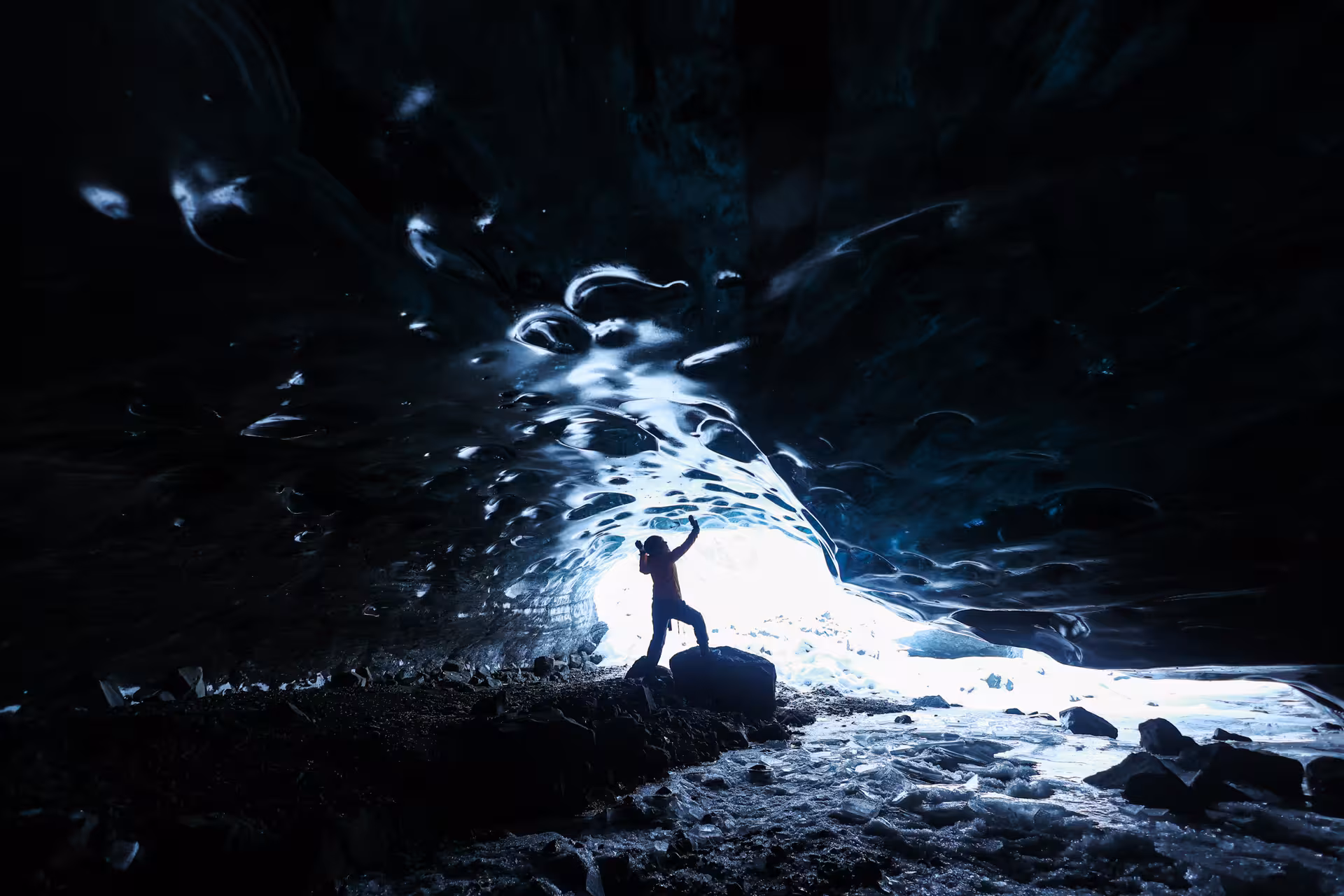 Solo explorer silhouetted at the entrance of a breathtaking Vatnajokull ice cave during a professional guided glacier tour in Iceland.