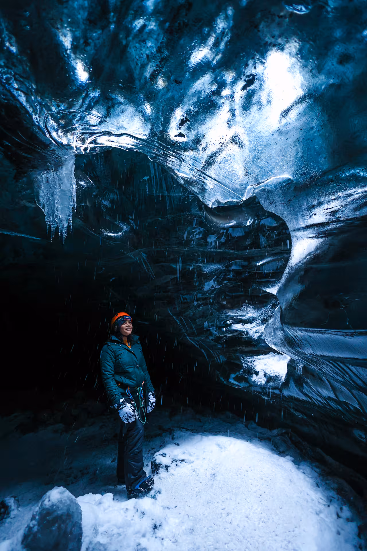 A smiling explorer in winter gear gazes up at stunning blue ice formations inside Vatnajokull glacier cave Iceland