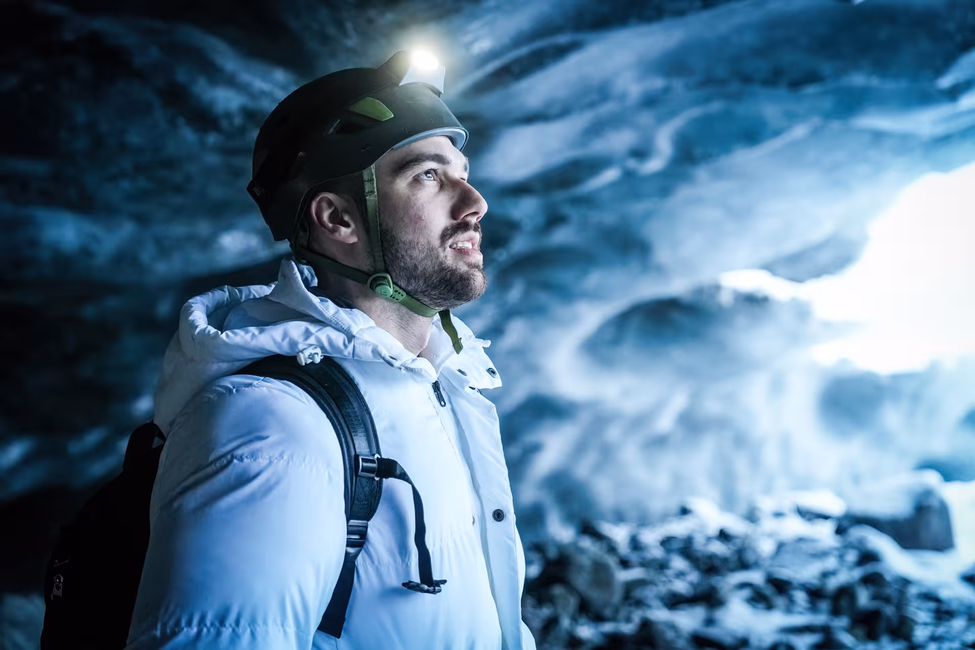 Male explorer with headlamp helmet looks in awe at breathtaking blue glacial walls during Vatnajokull ice cave guided tour