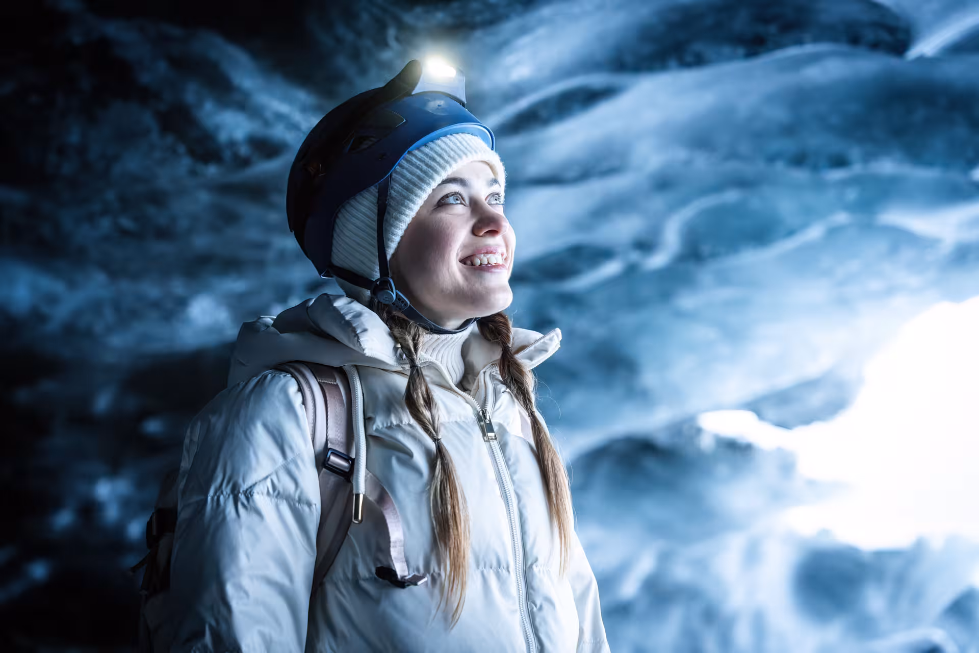 Smiling woman with helmet and headlamp exploring the stunning blue Vatnajokull ice cave on a guided tour in Iceland