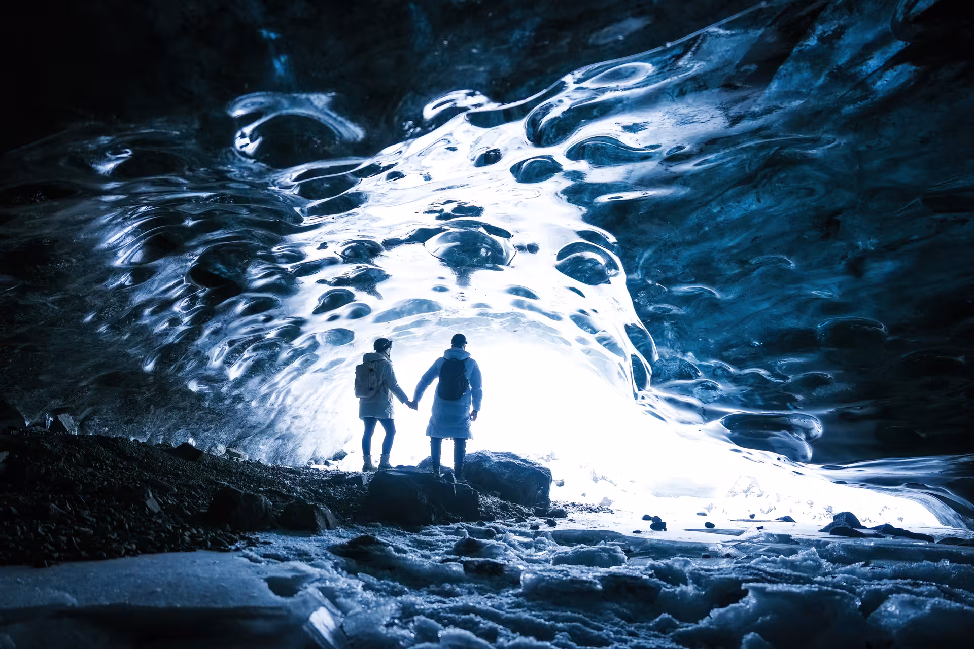 Couple holding hands silhouetted against the glowing entrance of a breathtaking Vatnajokull glacier ice cave in Iceland