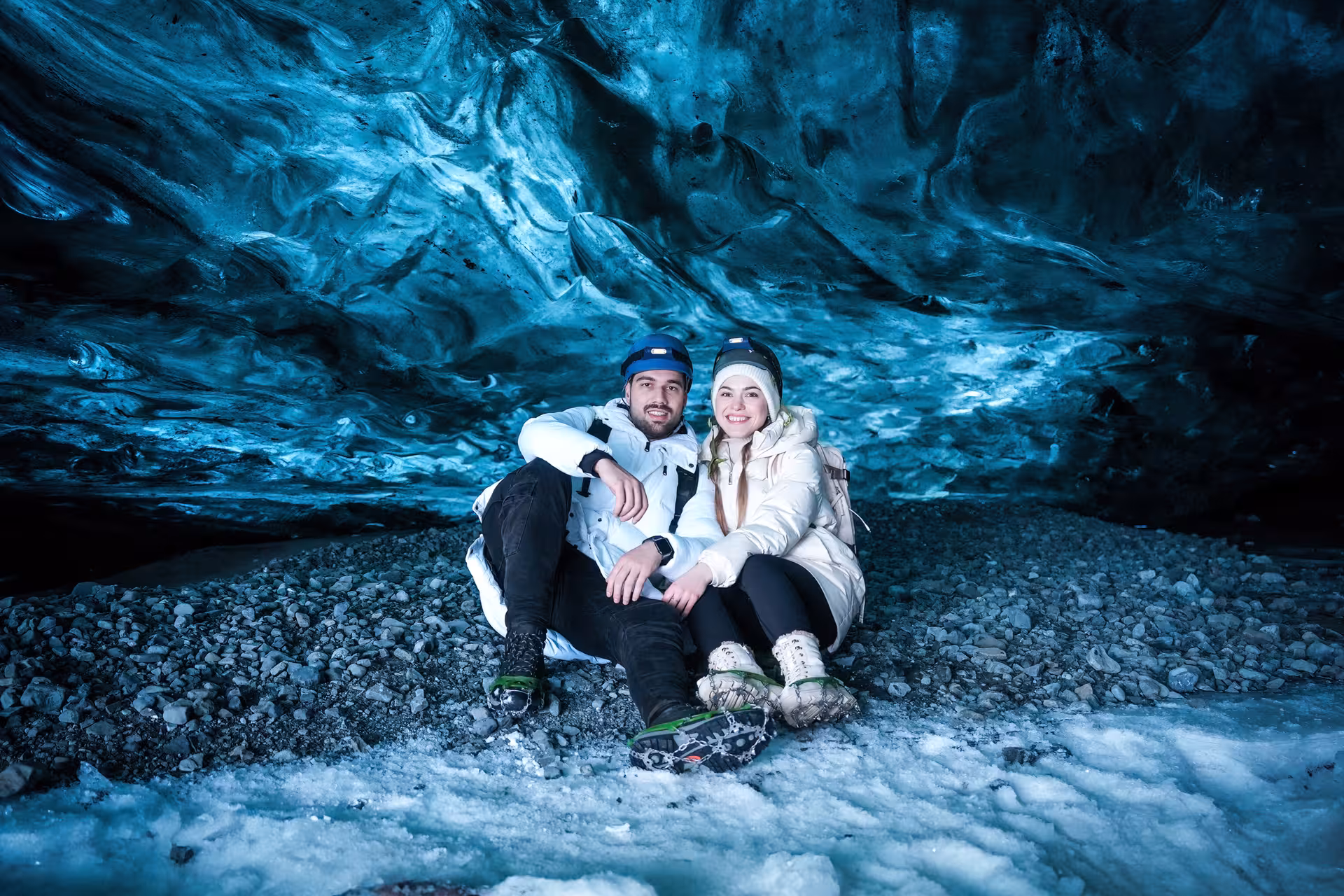 Happy couple sitting together inside the glowing blue Vatnajokull ice cave during a professional photo guided tour Iceland