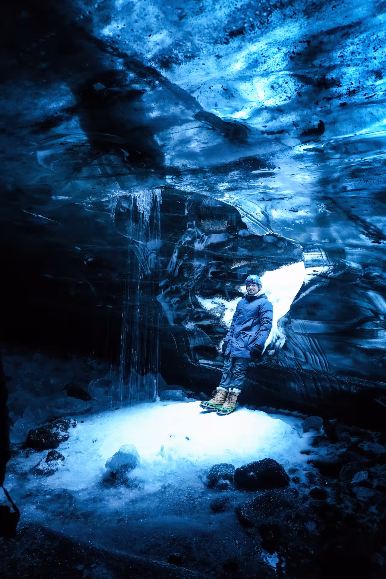 A smiling explorer stands beside a cascading ice waterfall inside the breathtaking blue Vatnajokull glacier cave Iceland