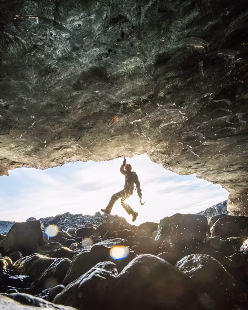 Silhouetted ice climber hanging with ice axe inside a glacier cave on a professional photo guide tour