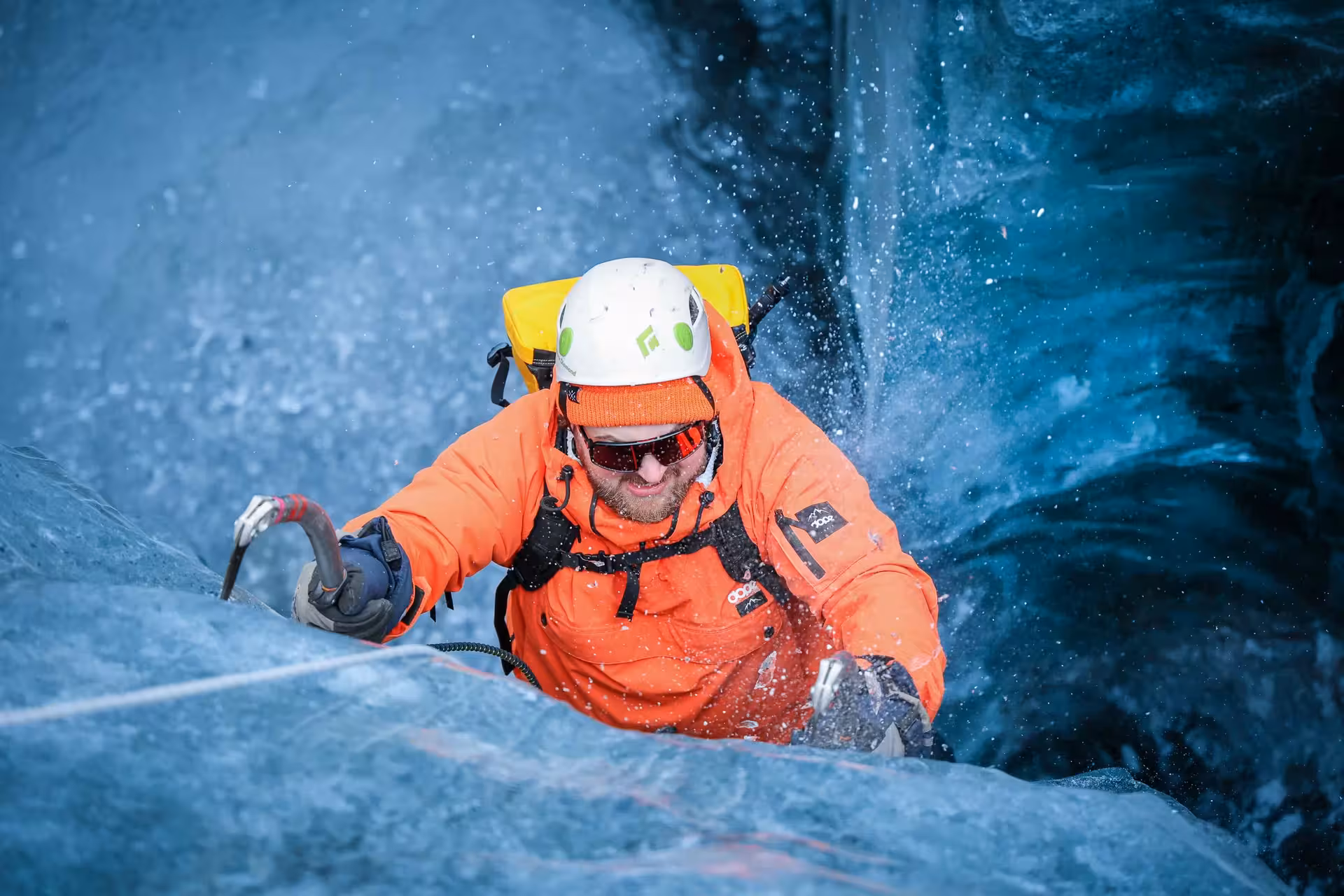 Expert climber in orange gear scaling a stunning blue glacier wall on a guided ice climbing tour