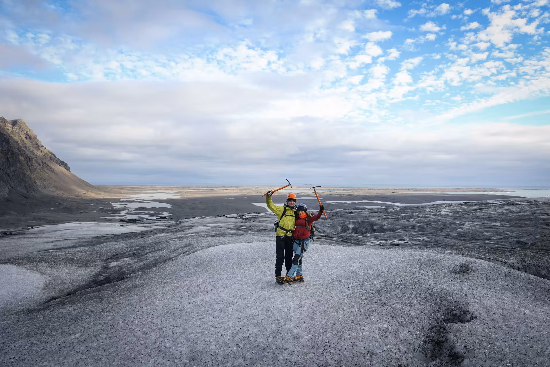 Two glacier ice climbers raising ice axes triumphantly on a vast Iceland glacier during a professional photo guide tour