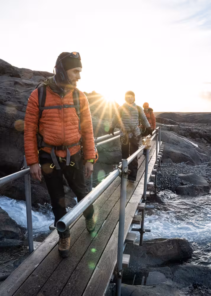 Glacier ice climbing tour group crossing a wooden bridge at sunset wearing harnesses and climbing gear