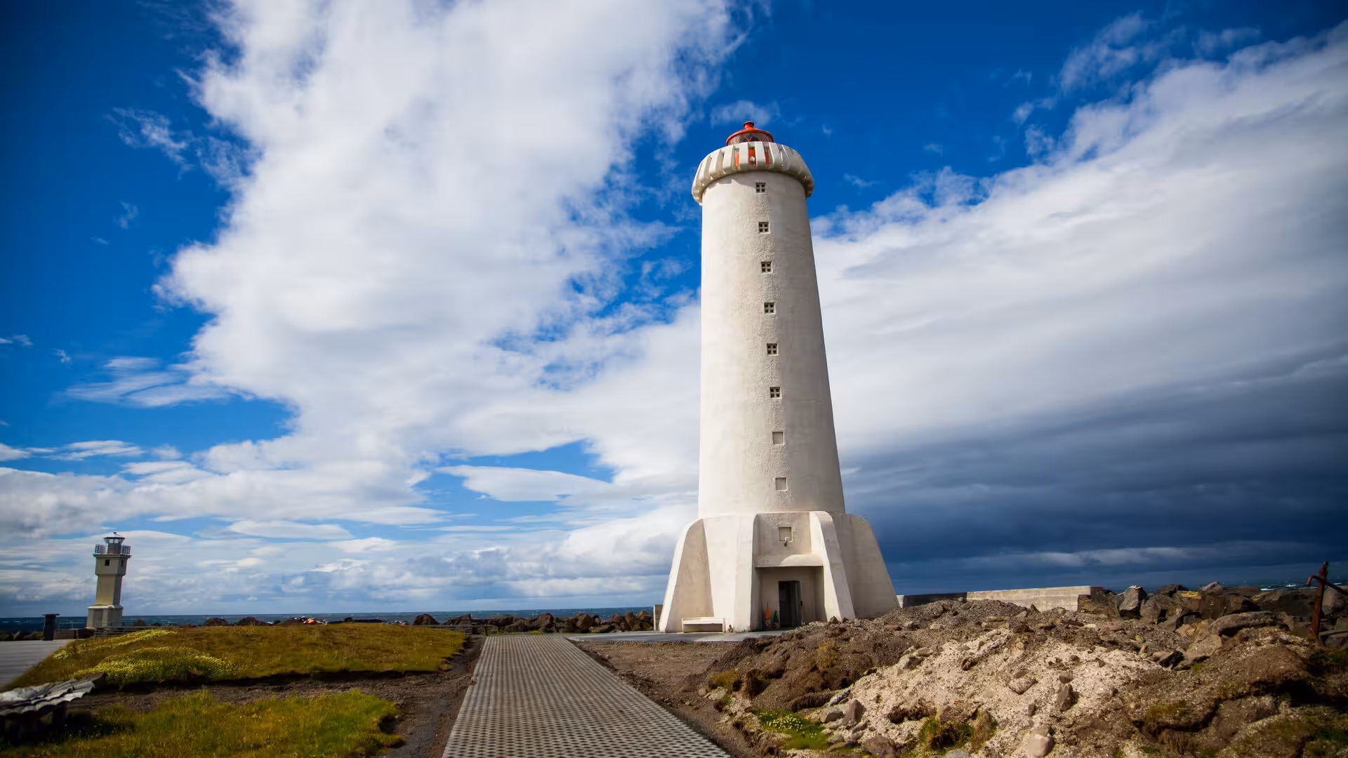 Iconic white Reykjavik lighthouse on rocky coastline under dramatic blue sky on Iceland elves nature driving tour