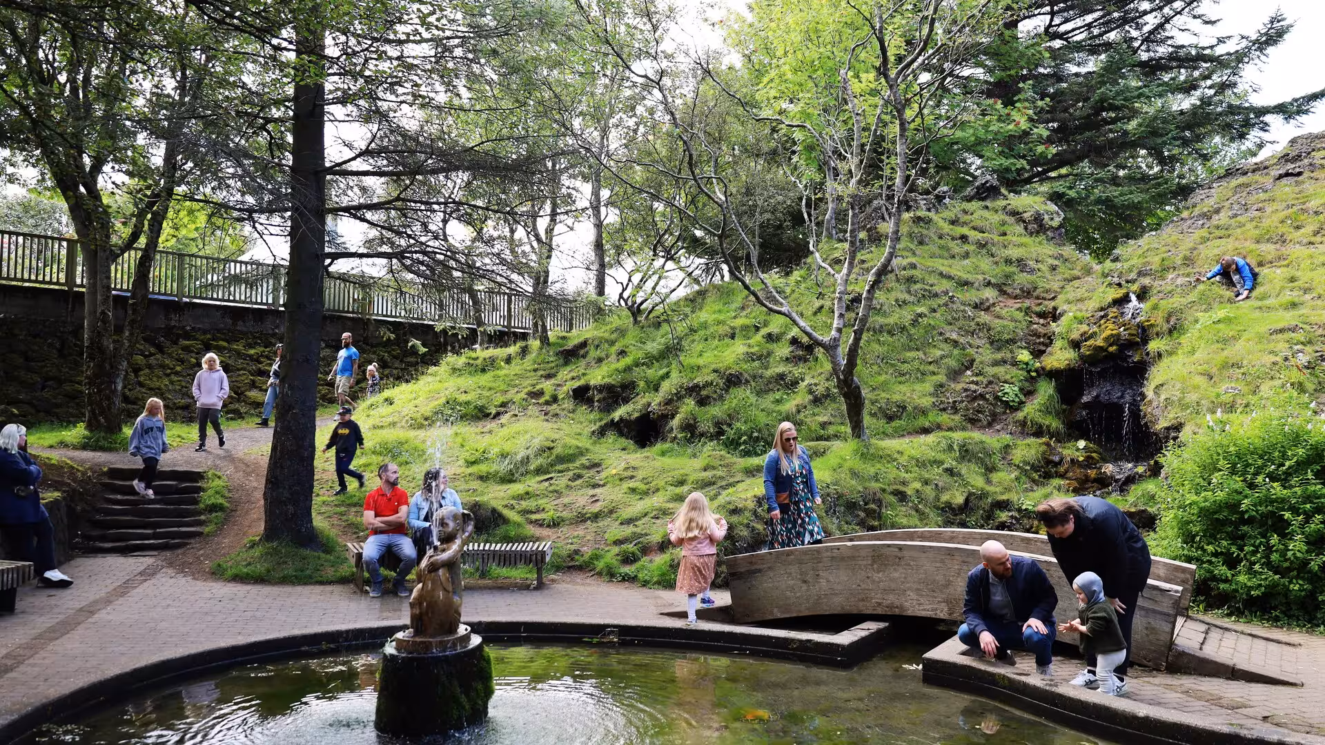 Visitors exploring lush green Reykjavik park with fountain and waterfall on guided Iceland elves nature driving tour