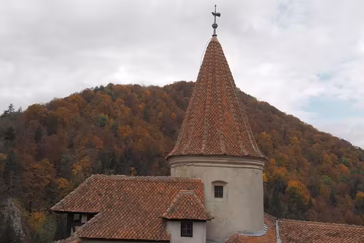Iconic Bran Castle tower with red-tiled conical roof set against autumn forest hills in Transylvania Romania
