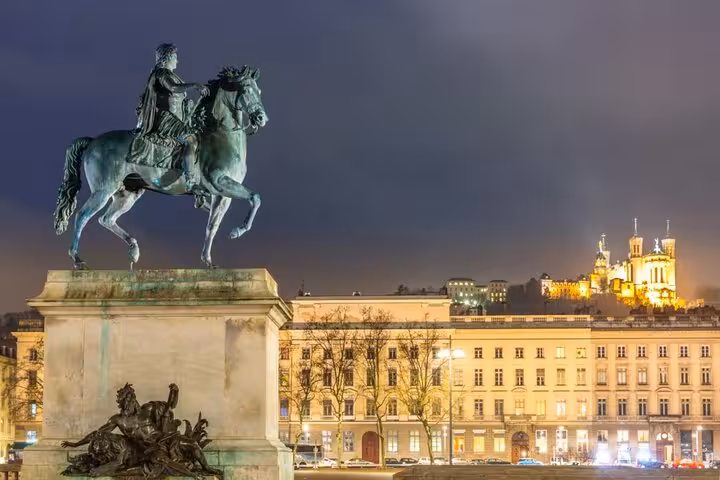 Iconic Lyon Place Bellecour equestrian statue lit up at night with Fourviere Basilica glowing on the hill backdrop