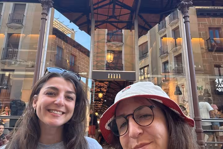Two smiling women taking a selfie outside Mercado de San Miguel during a self-guided walking tour in Madrid