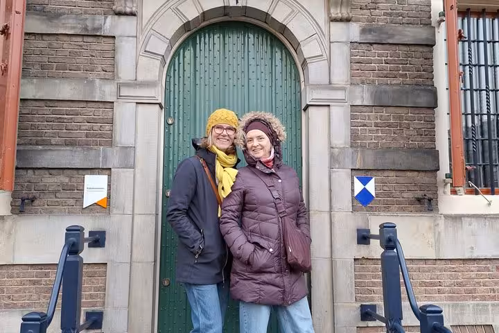 Two smiling women posing before a historic Amsterdam building during a self-guided escape game scavenger hunt tour