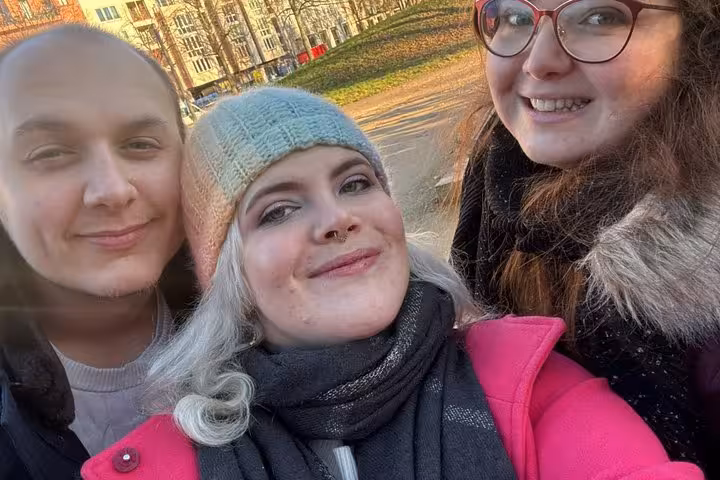 Three friends smiling on a Berlin WW2 self-guided walking tour exploring historic wartime sites with a smartphone app.