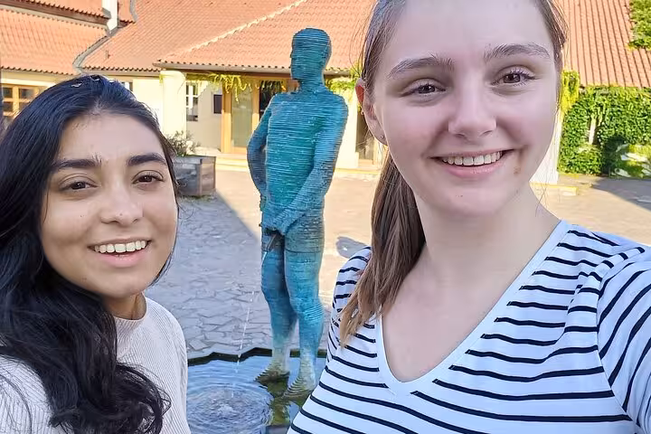 Two smiling women taking a selfie near a turquoise sculpture fountain on a Prague self-guided walking tour