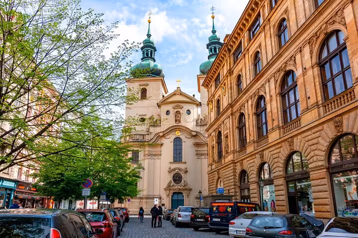 Prague self-guided walking tour passing a stunning Baroque church with green copper domes in the Old Town streets