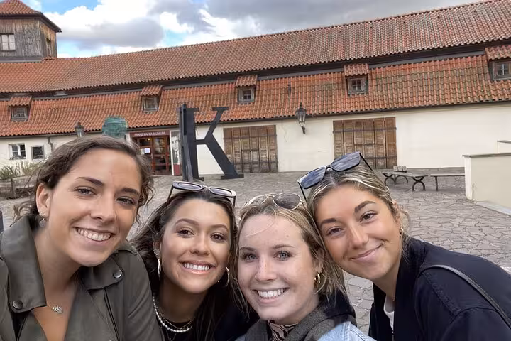 Happy group of friends enjoying Prague outdoor escape game selfie near historic Kafka Museum cobblestone courtyard