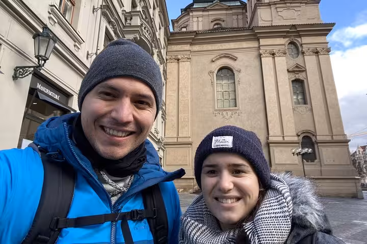 Smiling couple taking a winter selfie near a historic Prague church on a self-guided walking escape game tour