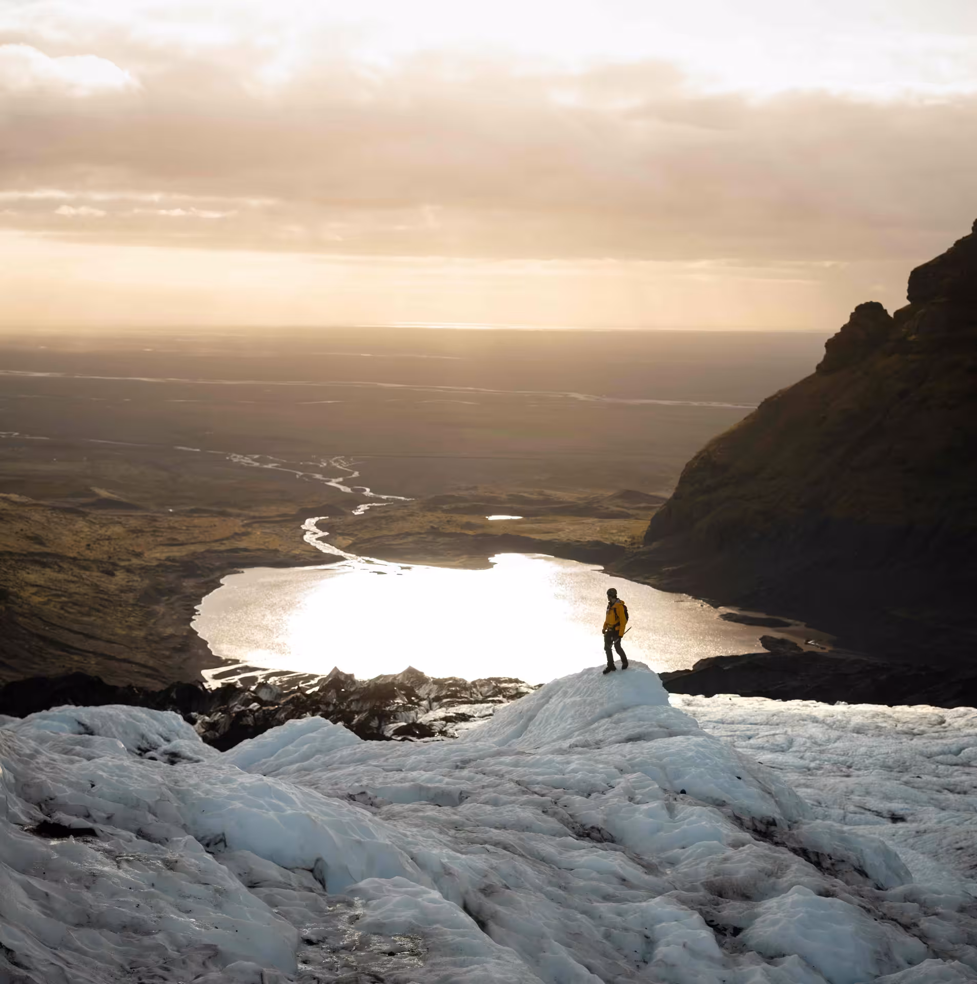 Solo hiker in yellow jacket standing on Falljokull Glacier edge with stunning panoramic Skaftafell Iceland landscape at golden hour