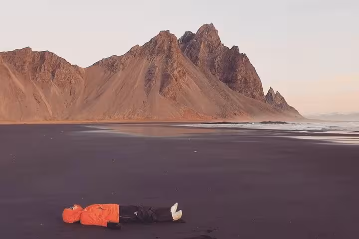Photographer lying on black sand beach with dramatic Vestrahorn mountain backdrop in southeast Iceland