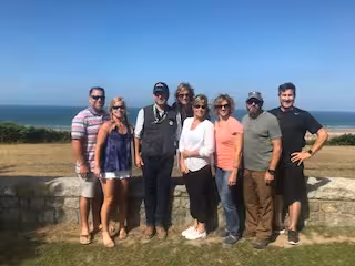 Group of five tourists taking a selfie at Normandy beach near a metal sculpture on a D-Day tour