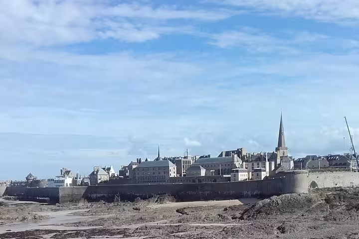 Group of four tourists posing at rocky coastline with historic stone chapel at St Malo, Brittany
