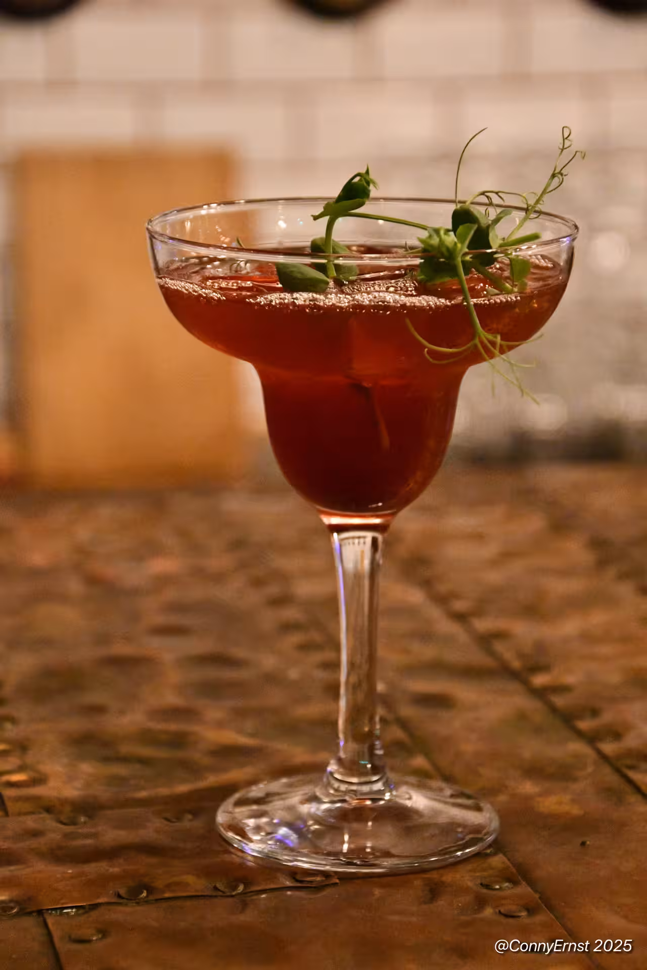 Deep red cocktail in crystal coupe glass garnished with fresh pea shoots, served at Reykjavik dining experience