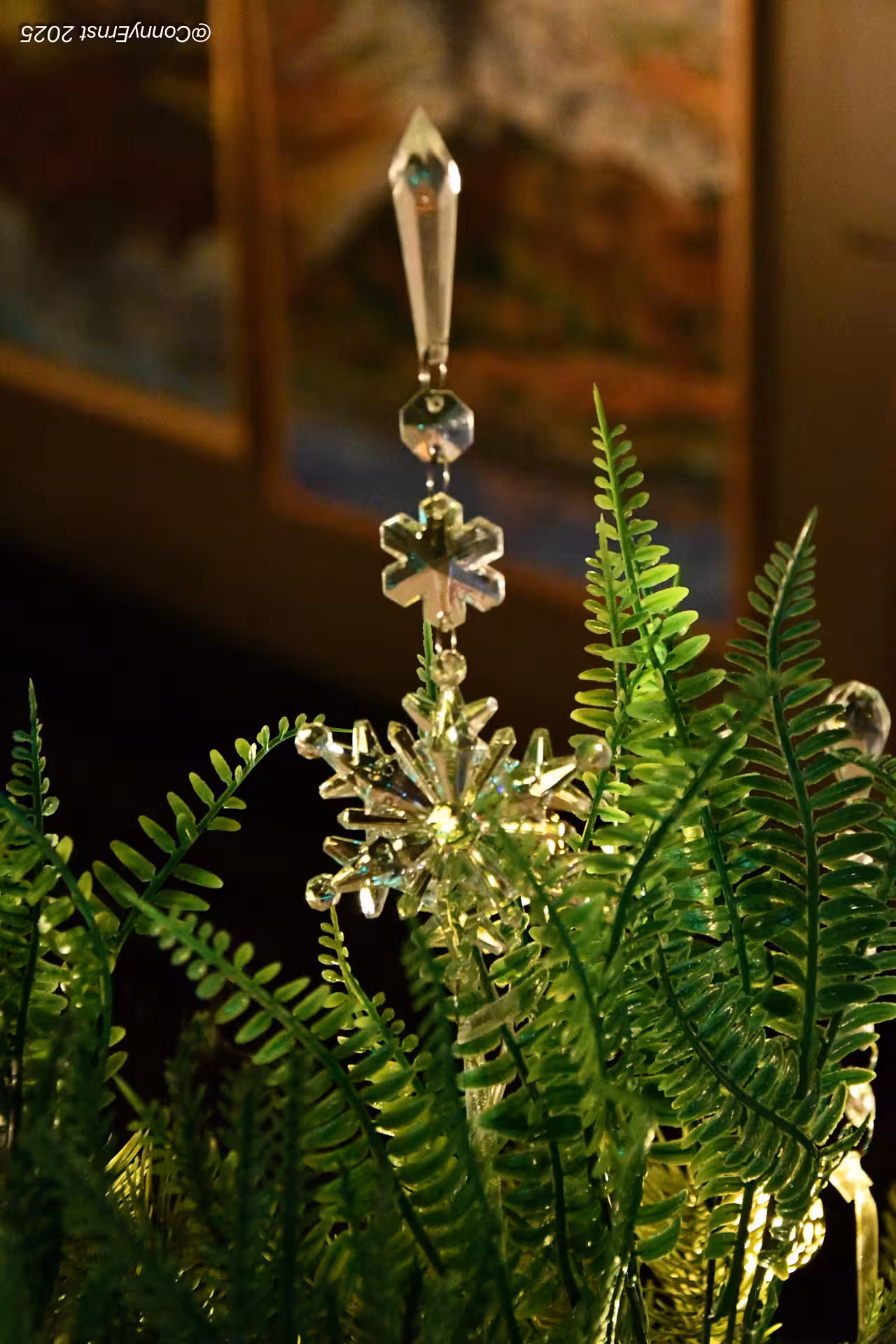 Crystal snowflake ornament hanging among green fern leaves with warm bokeh lighting