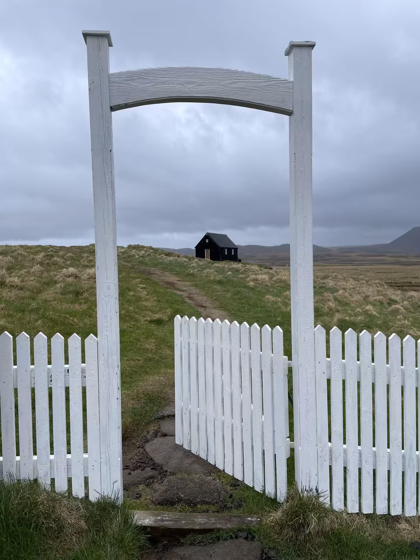 White picket fence gate entrance with green meadows and black building on Reykjanes Peninsula, Iceland