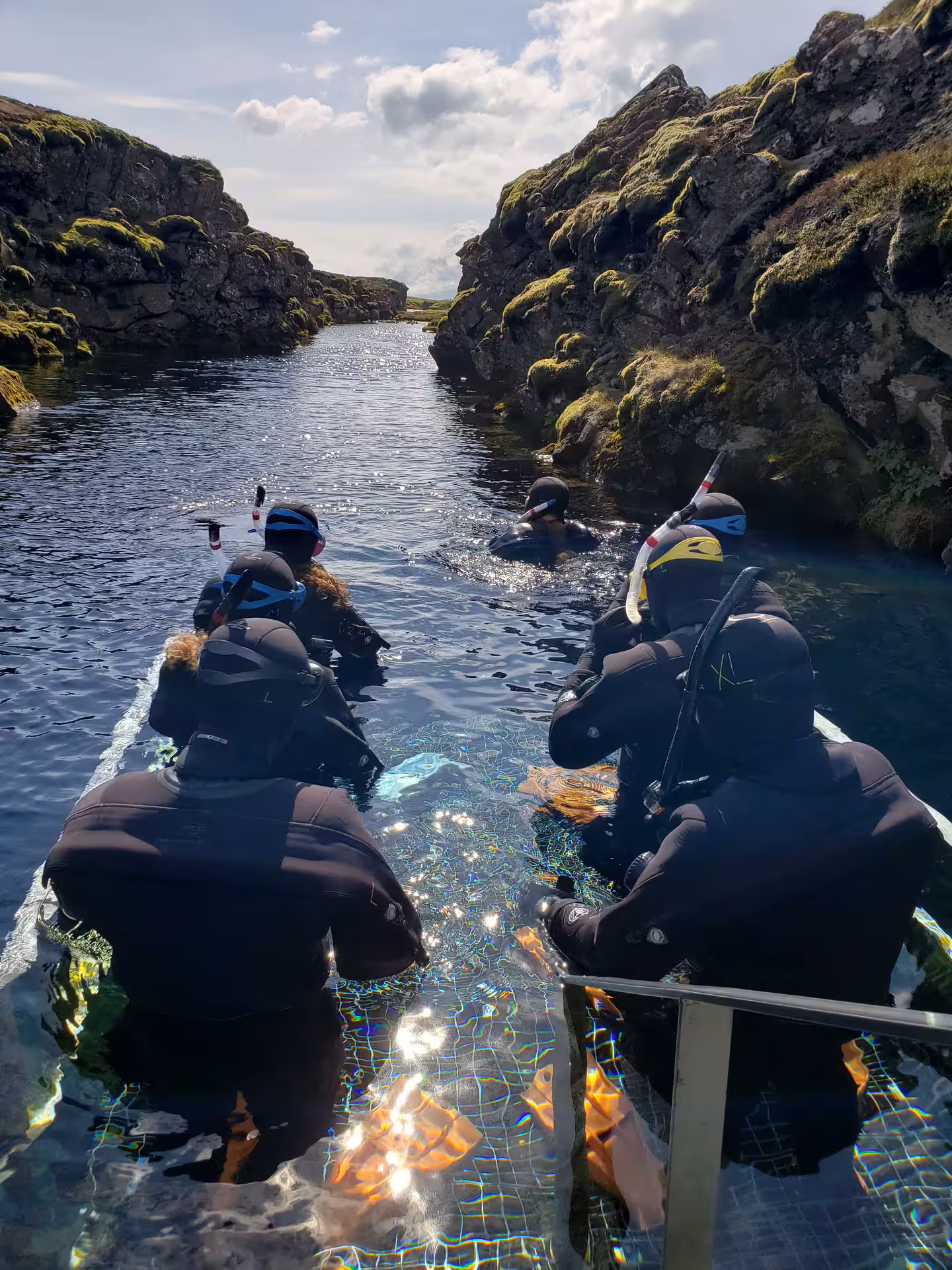 Snorkelers in wetsuits entering crystal clear water at Silfra fissure, Thingvellir Iceland