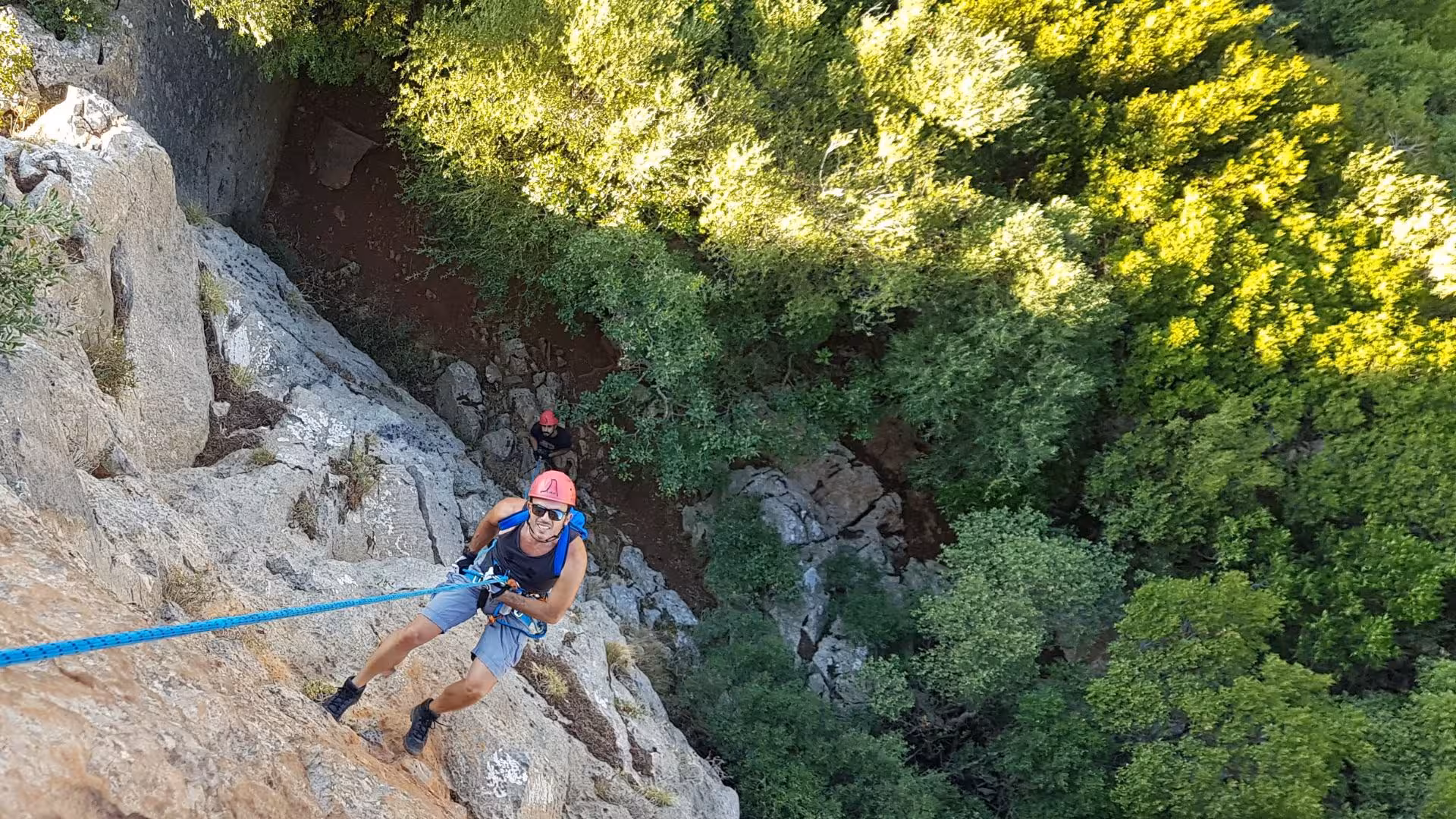 Adventurer abseiling down the rocky cliffs of Gutturu Xeu canyon surrounded by lush greenery in Iglesias, Sardinia.