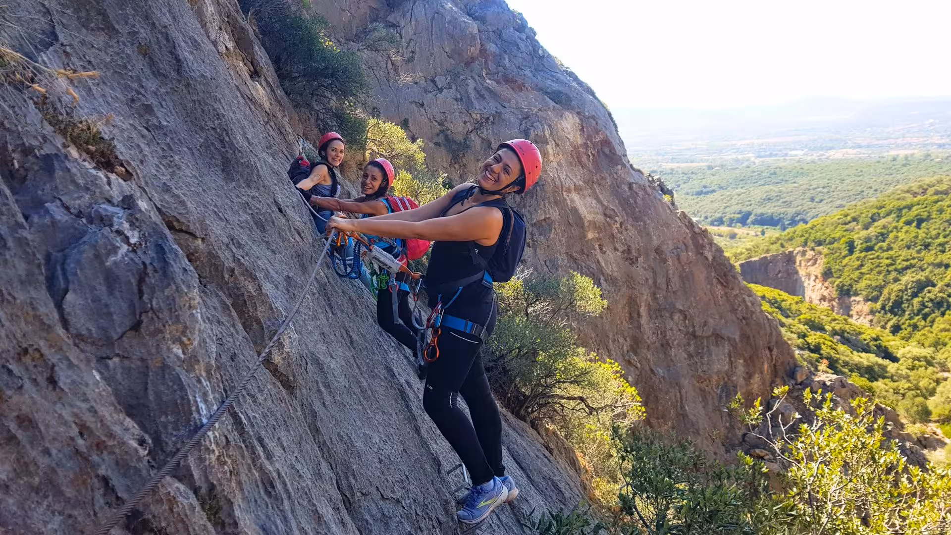 Group of climbers smiling while ascending a steep cliff in Gutturu Xeu canyon, Iglesias, perfect for adventure seekers.