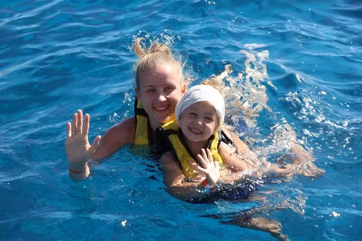Family snorkeling in Red Sea wearing life jackets on Abu Dabab Bay turtle swim tour from Hurghada