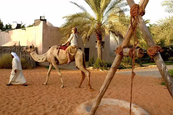 A visitor rides a camel beside a local guide in the sandy landscape of Abu Dhabi on a 4x4 tour from Dubai.