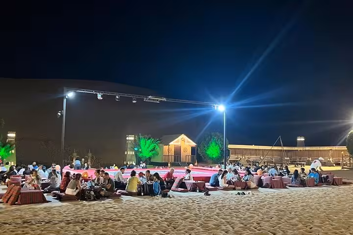Guests enjoying open-air BBQ dinner seating under bright lights at Abu Dhabi desert safari live show night event