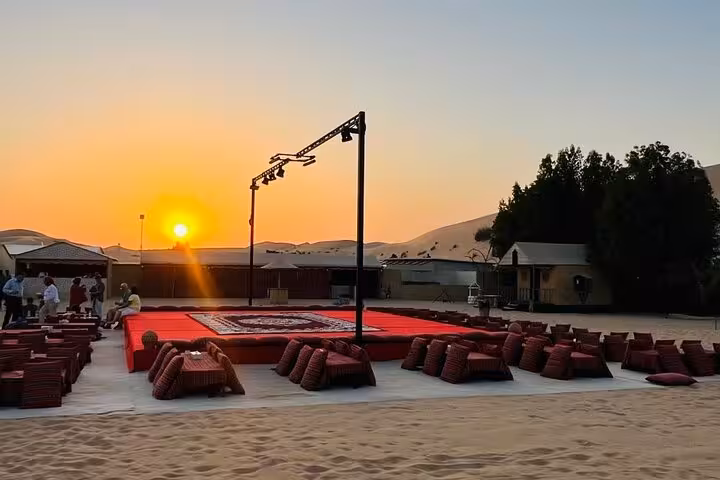 Traditional Arabian desert camp setup with cushioned seating and stage at sunset for Abu Dhabi BBQ dinner live show